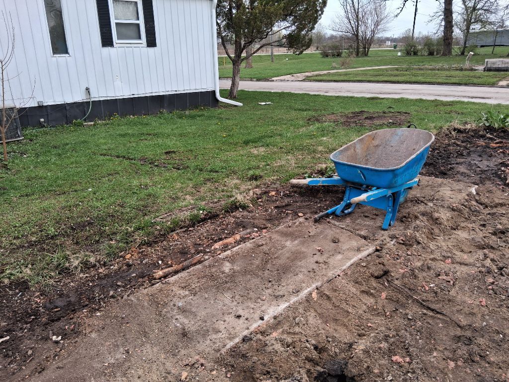 Blue wheelbarrow on a dirt path beside a house and grassy yard.