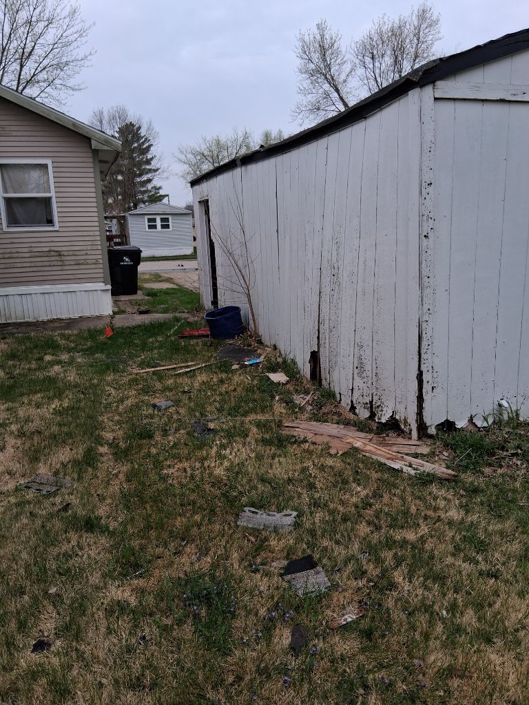 Narrow grassy path between two houses, with a white weathered fence and overcast sky.
