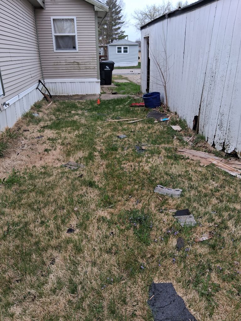 Narrow backyard walkway between house and fence with patchy grass and scattered stepping stones.