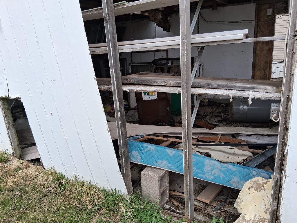 Damaged shed shelving with scattered debris and a blue board inside a partially broken wall