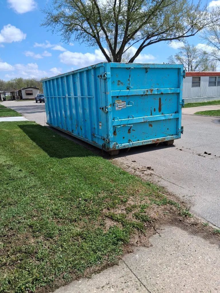 Blue shipping container sitting on grass beside a paved road under trees