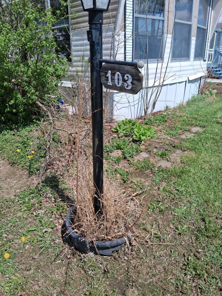 Black mailbox post with house number 103 beside a white house and grassy yard.