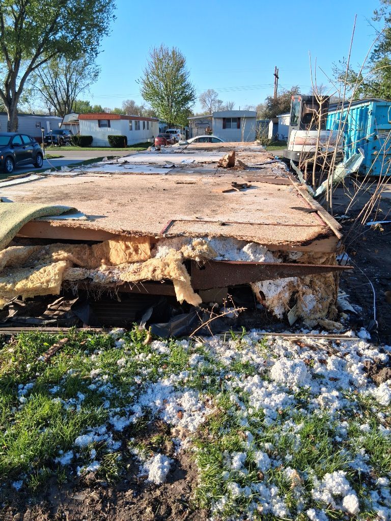 Collapsed roof/debris in a yard with scattered snow and homes in the background