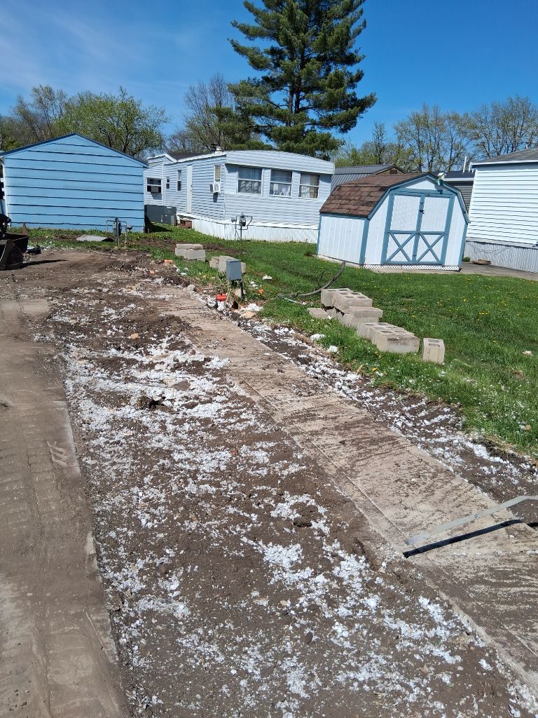Snow-dusted dirt driveway beside blue sheds and a white mobile home under a clear sky