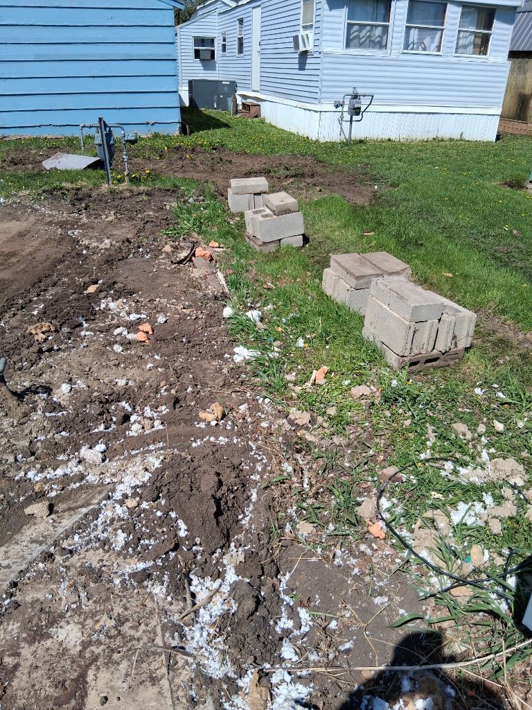 Backyard construction site with dirt pile, concrete blocks, and a blue house in the background