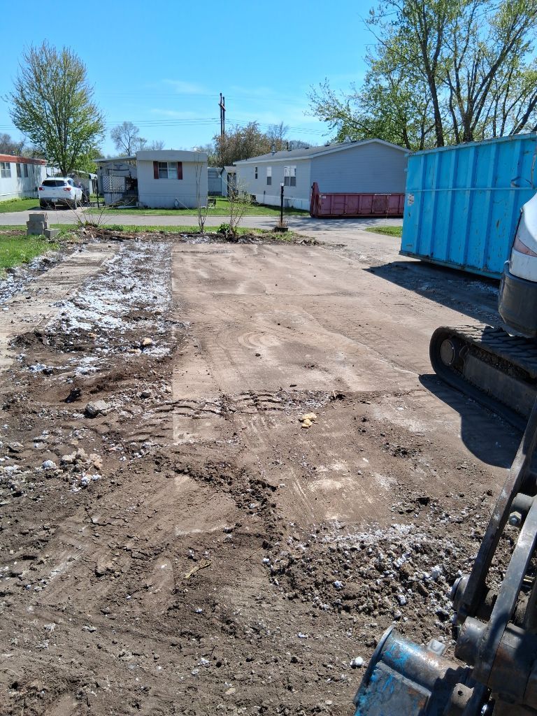 Dirt driveway beside a blue dumpster and small houses on a sunny day