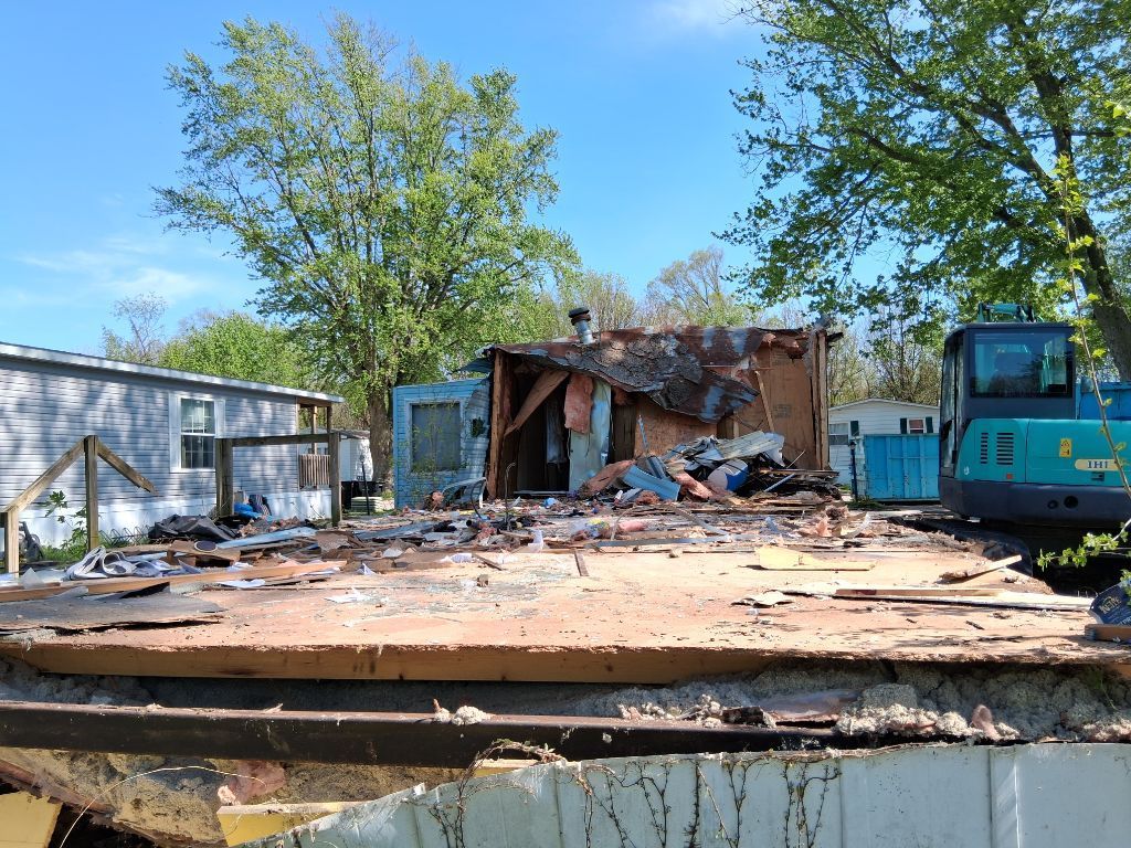 Demolition site with a collapsed house, scattered debris, and blue machinery under a clear sky