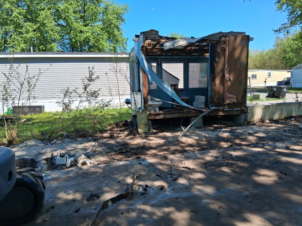 Burned-out mobile home with charred frame and debris in a yard after a fire