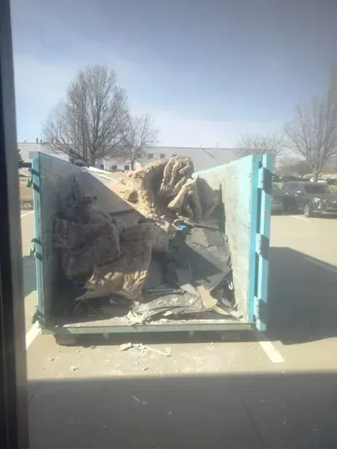 A light blue, open-top dumpster in a parking lot, partially filled with construction debris and beige insulation material.