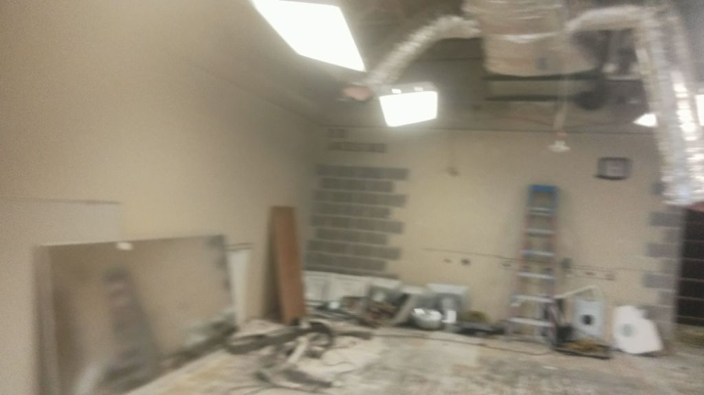 Construction room with drywall tools, ladders, and debris under ceiling lights