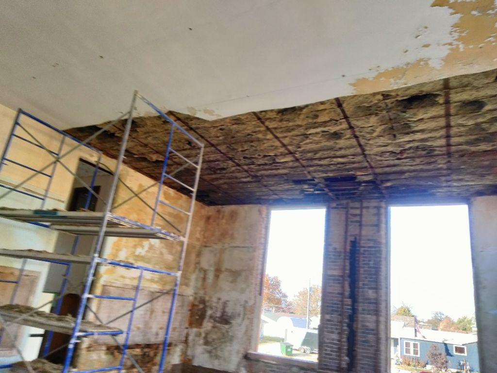 Renovating room with scaffolding, exposed ceiling, and two tall open windows overlooking rooftops