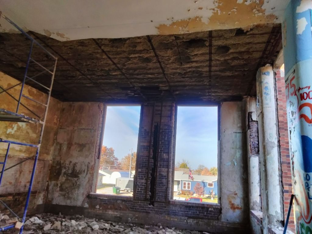 Damaged interior of an unfinished building with exposed ceiling and large open window openings.