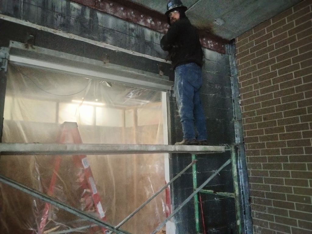 Worker standing on scaffolding inside a brick building, installing or repairing the ceiling.