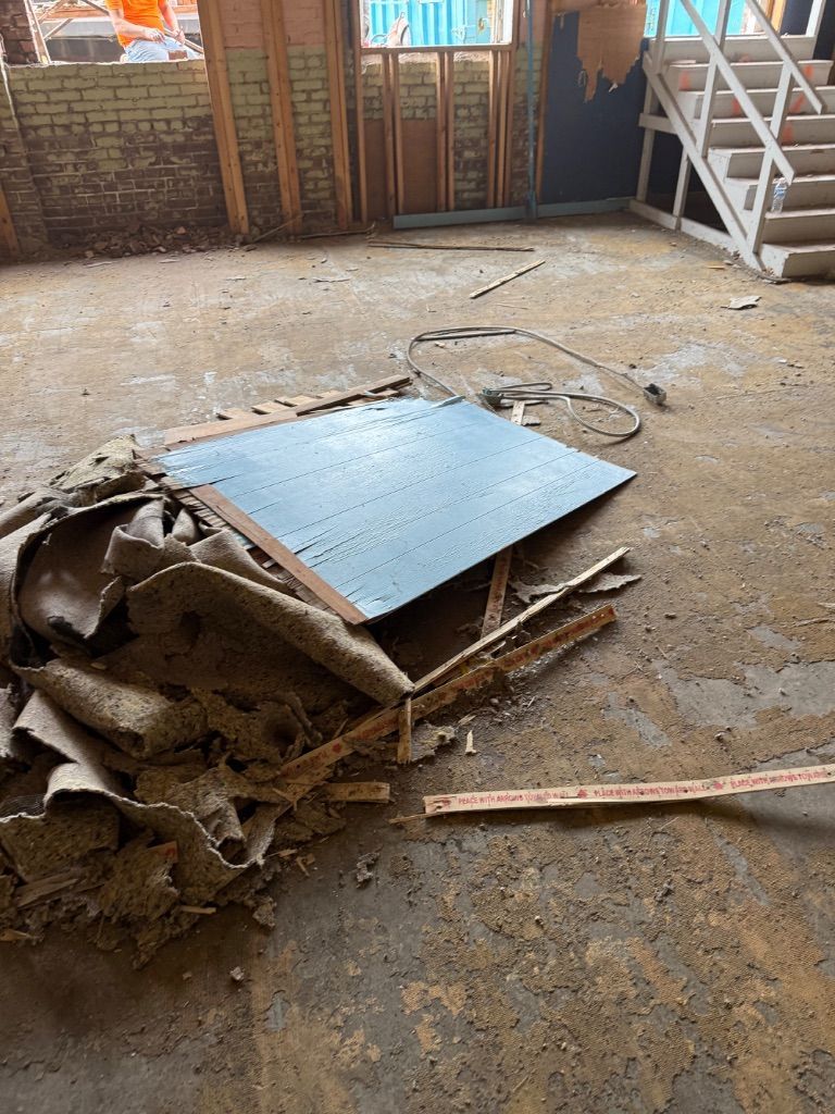 Damaged floor with a torn rug, broken wood, and a blue panel in a garage-like interior.