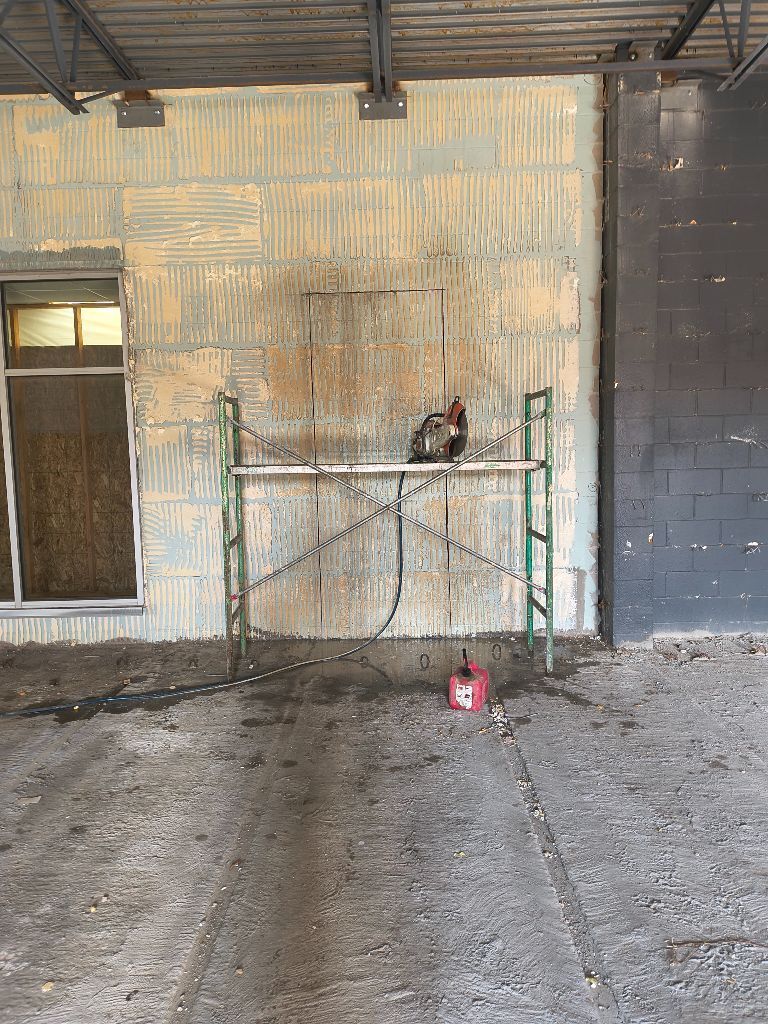 Worker on a scaffold beside a worn wall, with a red can on the ground below.