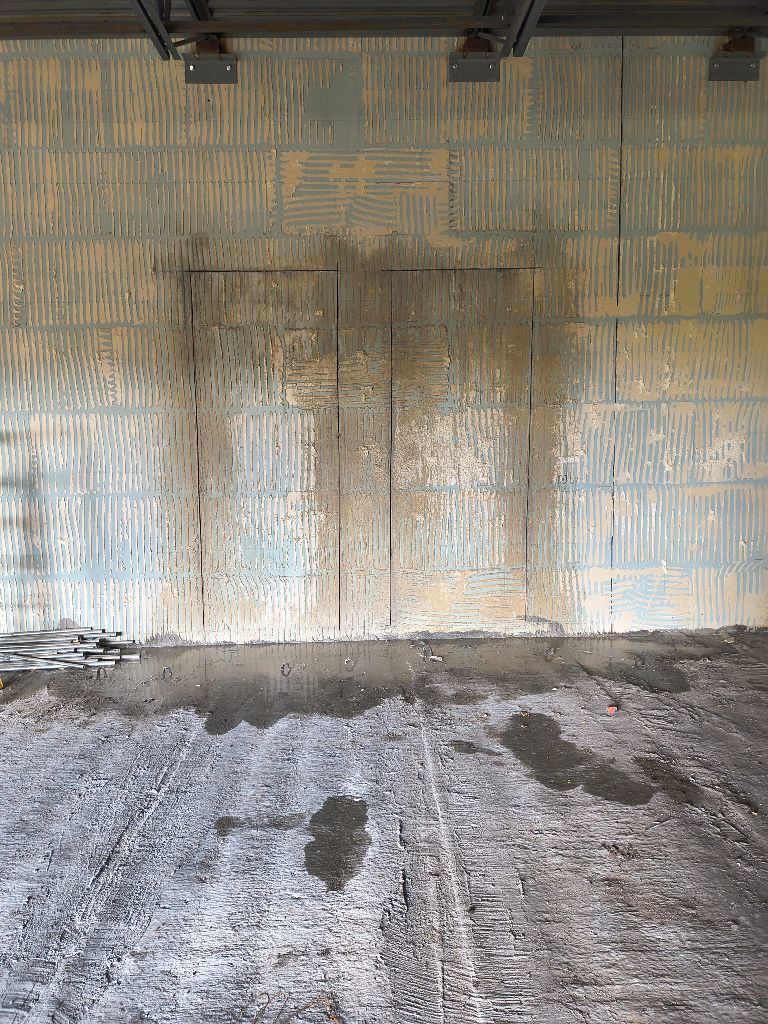 Weathered warehouse wall with a central door and stained concrete floor under an overhang