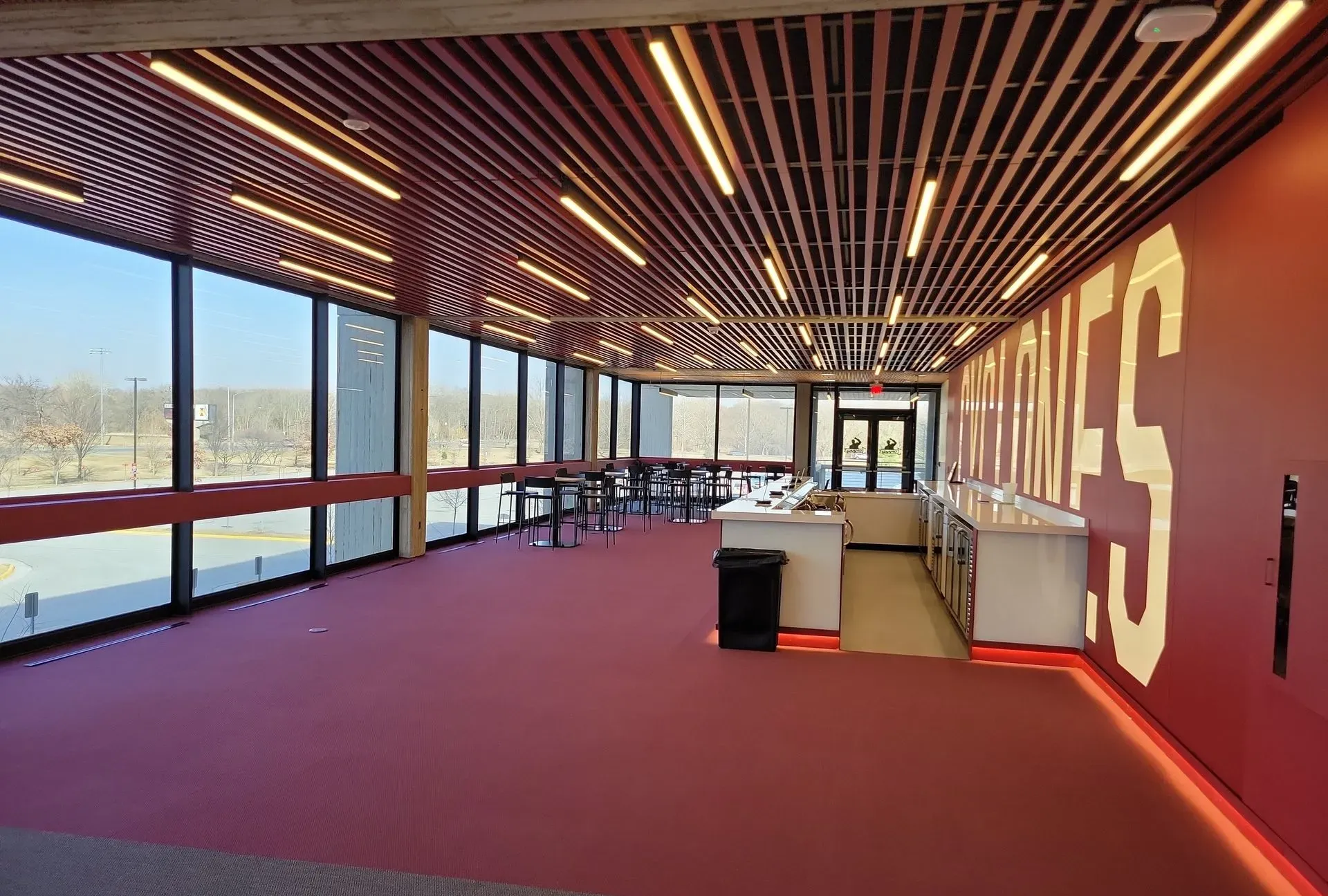 A modern room with red carpeting, wood-slatted ceiling, large windows, and a counter with the text 