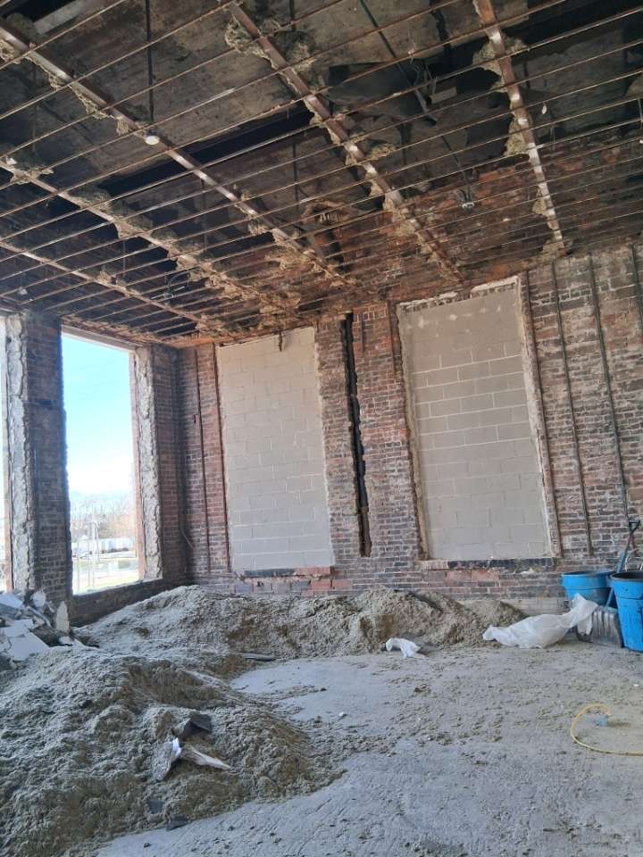 Construction site interior with exposed ceiling, brick walls, and piles of sand and debris on the floor