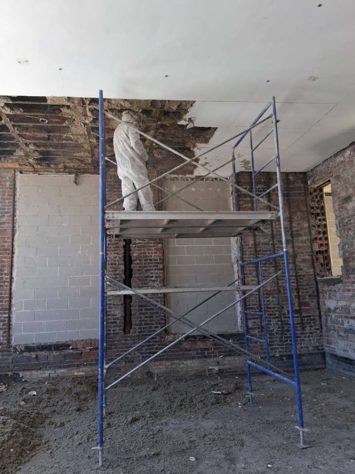 Worker on scaffolding repairing a damaged ceiling in an unfinished room