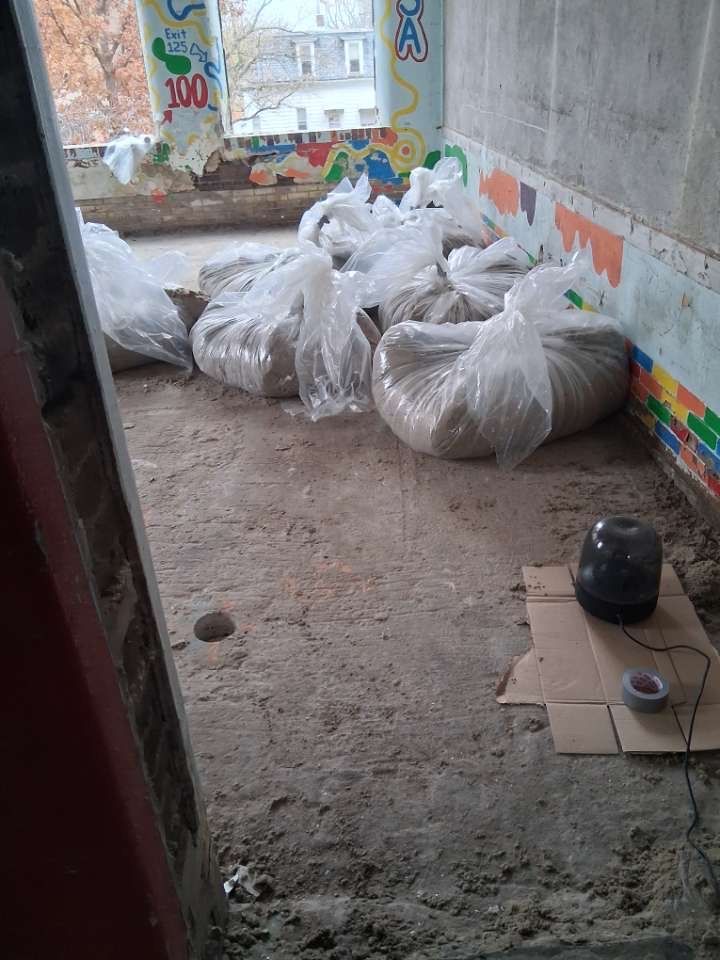 White plastic bags piled on a concrete floor beside a gray wall and open doorway.