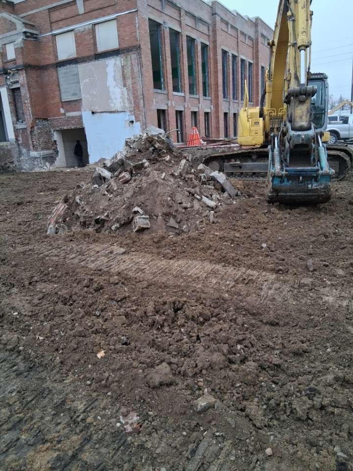 Construction site with excavator beside a dirt pile near a brick building under renovation