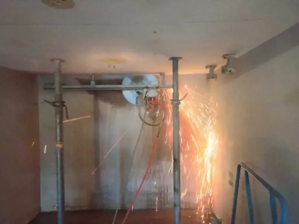 An industrial saw mounted on scaffolding cutting into a concrete wall, producing a spray of bright orange sparks.