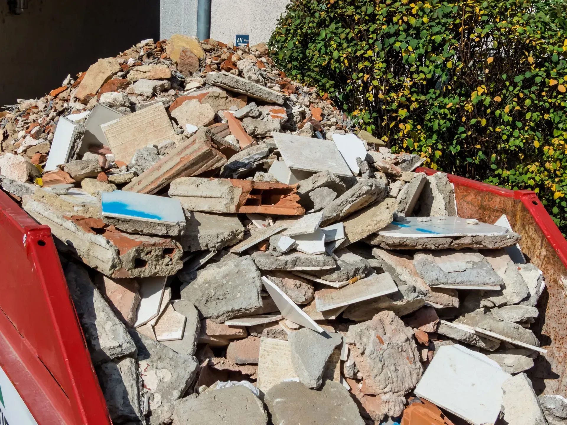 A pile of broken concrete, bricks, and construction debris inside a red metal dumpster outdoors.