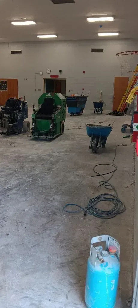 Interior view of a workshop with floor cleaning machines, utility carts, a propane tank, and coiled cables on the floor.