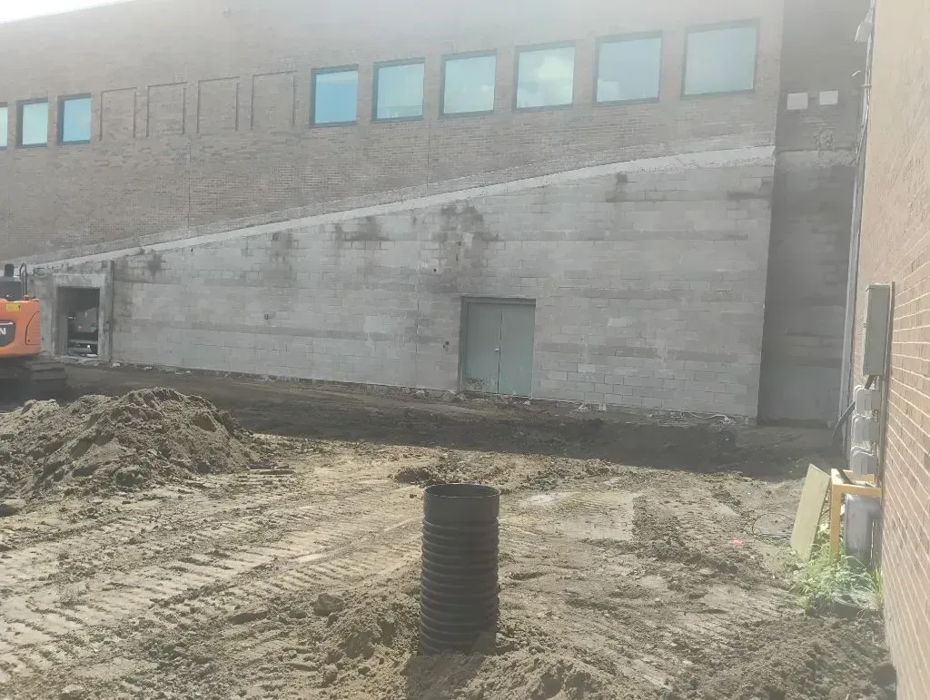 Construction site featuring a multi-story brick and concrete building with a row of windows, mud, and a black drainage pipe.