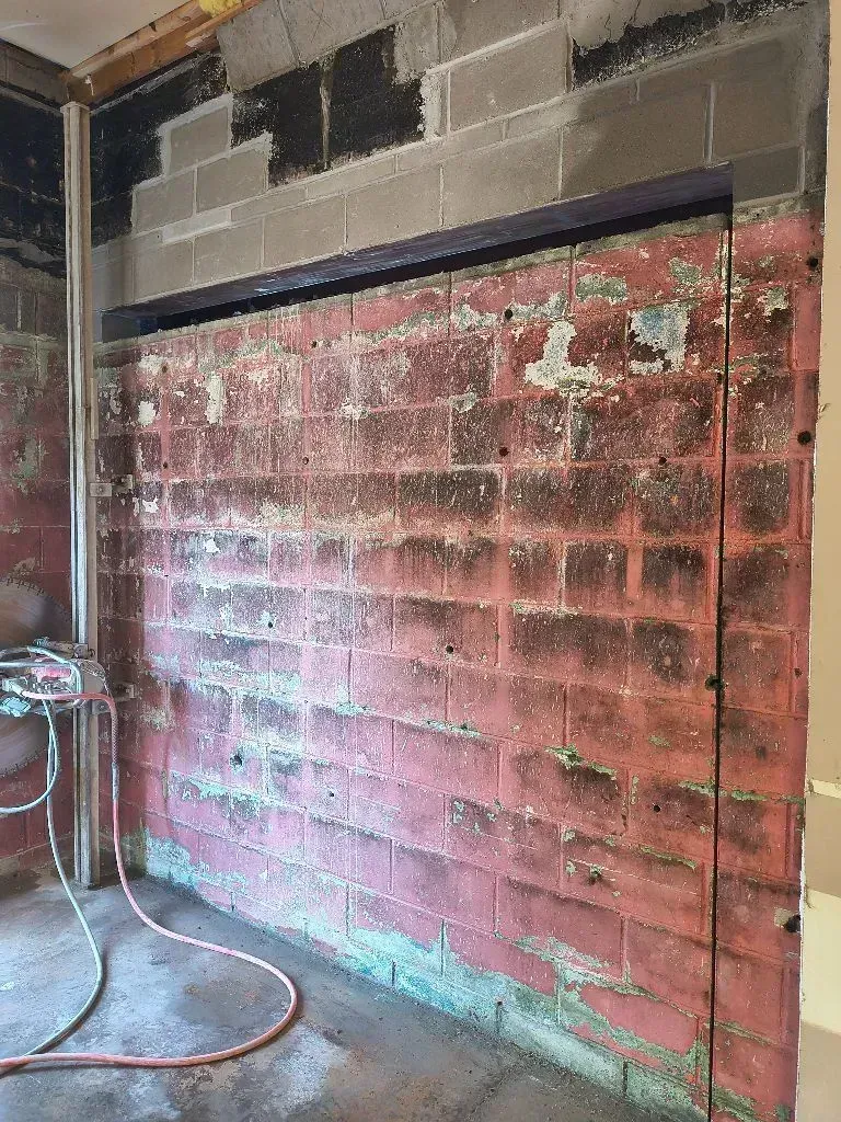 Interior view of a red brick wall under construction with an exposed steel lintel, adjacent to a metal pipe.