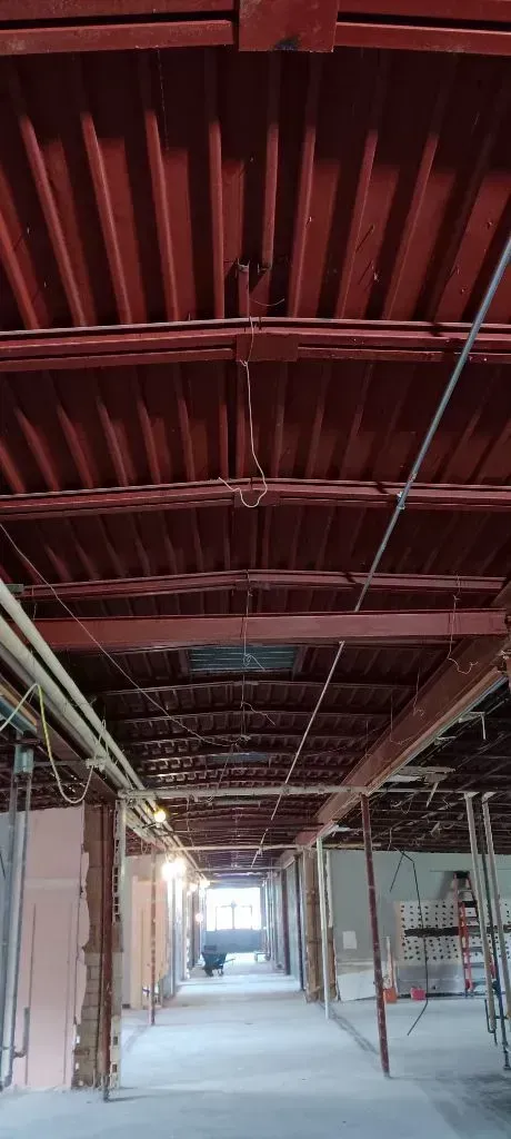 Interior view of a building under construction featuring exposed, deep red ceiling beams and a concrete floor.