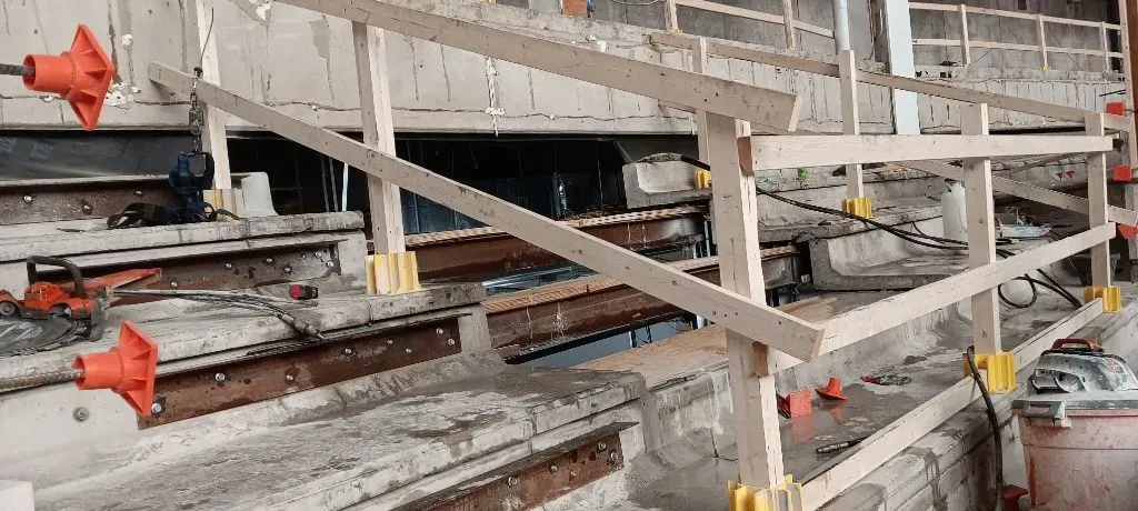 A temporary wooden safety railing installed along concrete stadium steps at a construction site.