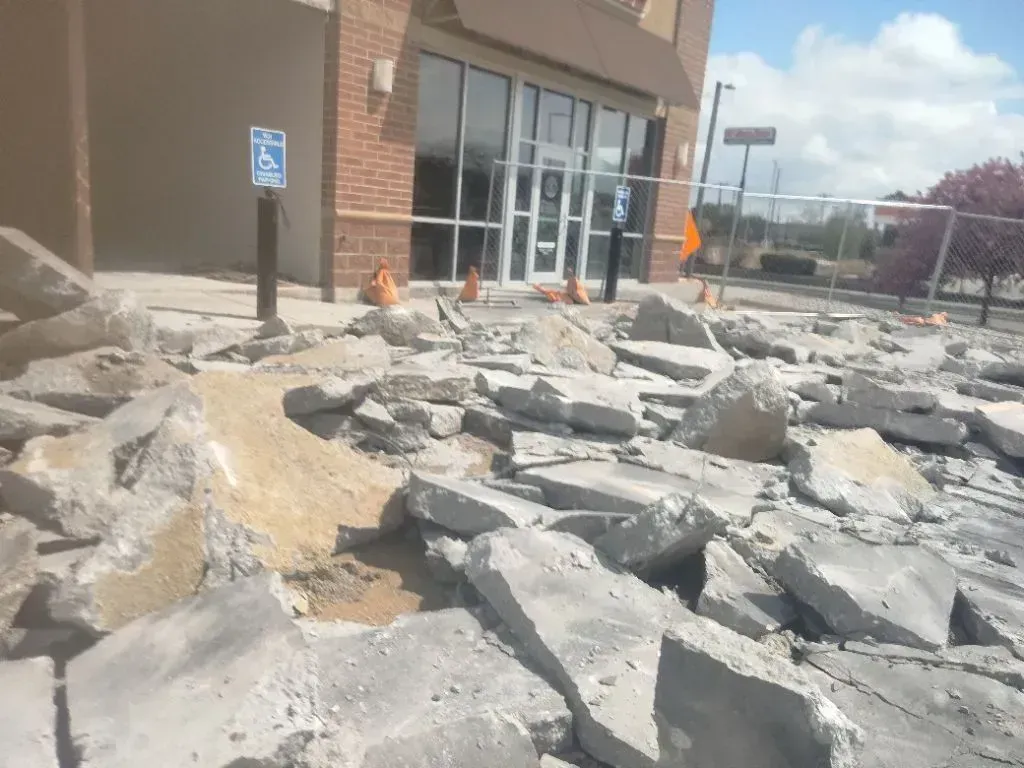 Construction rubble and broken concrete slabs covering the ground in front of a storefront building.