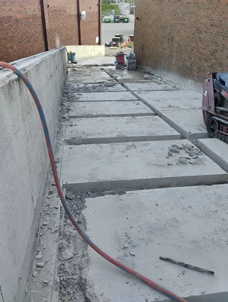 A construction site showing concrete slabs with narrow gaps cut into them along a wall, next to a piece of machinery.