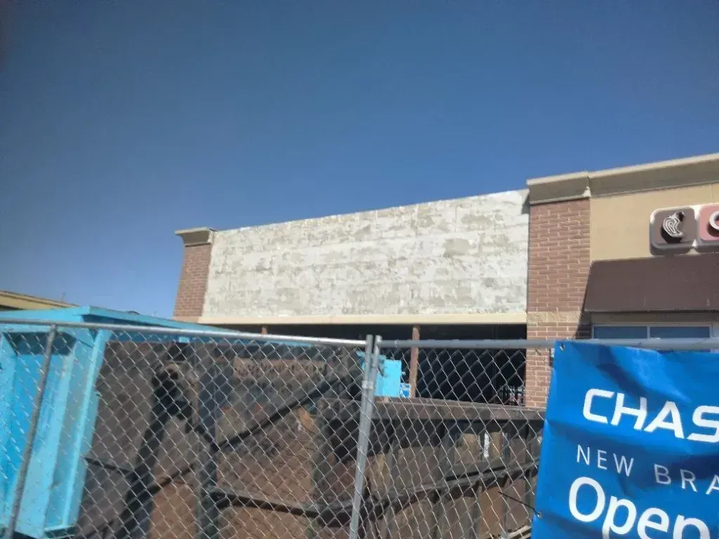 A Chase bank building under construction with a weathered white facade and a chain-link fence in the foreground.