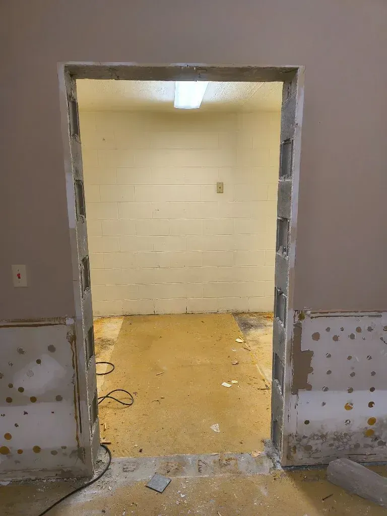 A doorway with no door, showing a small, unfinished room with beige concrete block walls and a dusty floor.