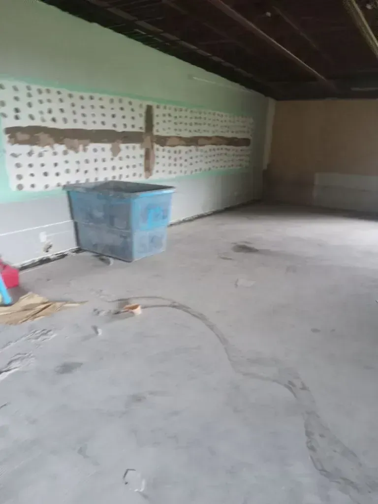 An unfinished interior room with gray concrete floors, a blue plastic bin, and a wall featuring a horizontal taped pattern.