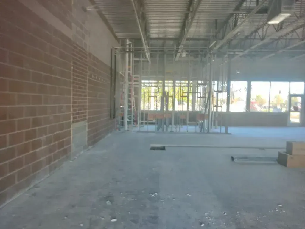 Interior view of a commercial space under construction with exposed brick walls, metal framing, and large windows.