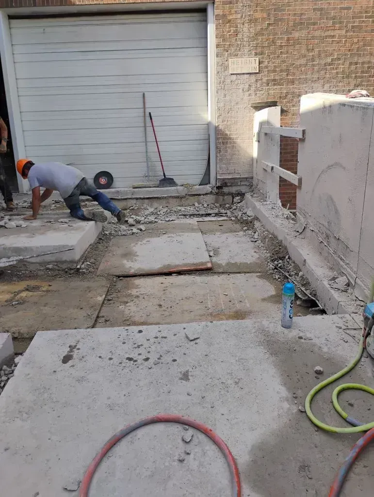 A construction worker in a hard hat kneeling on a concrete driveway while working on a residential exterior renovation.