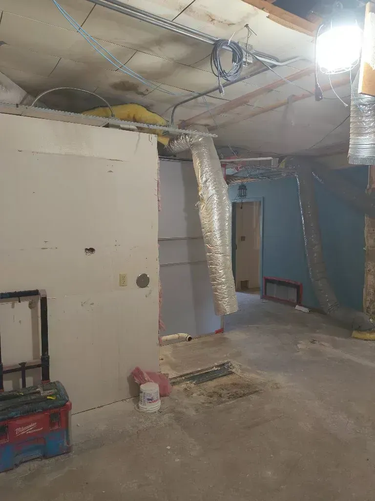 An unfinished room with exposed ceiling joists, silver ventilation ducts, drywall panels, and a red toolbox on the floor.
