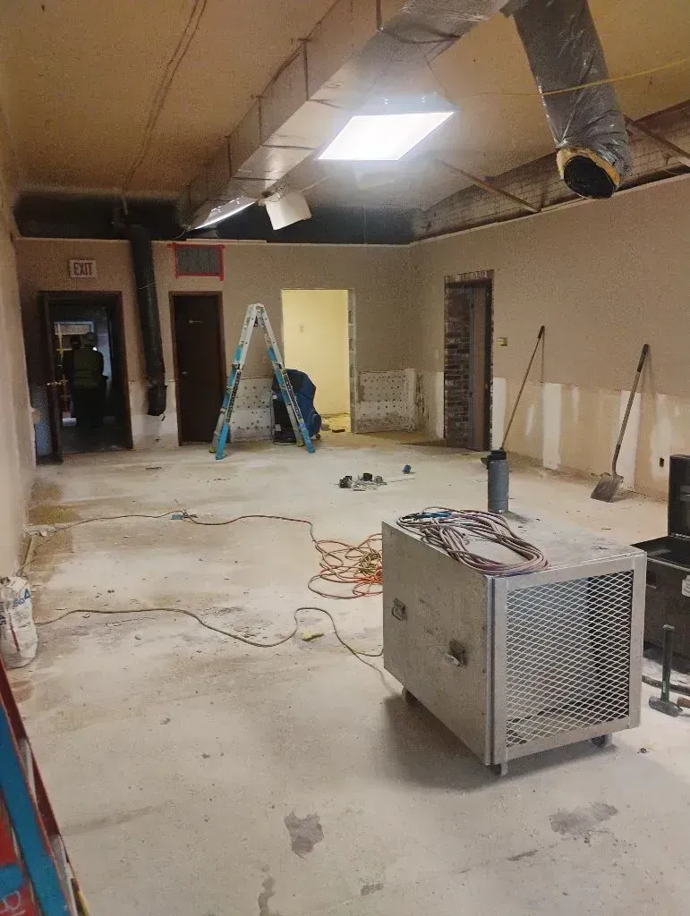 A room under renovation with exposed ductwork, a portable air scrubber in the foreground, and a ladder in the background.