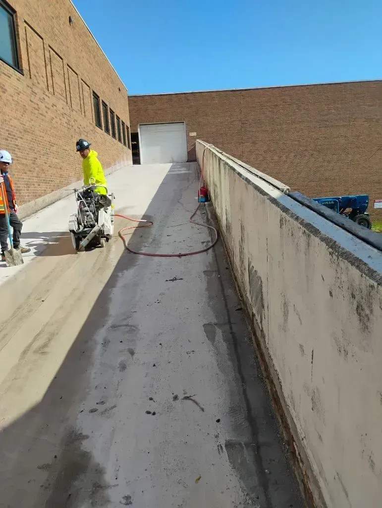 Two workers in high-visibility gear operate a concrete saw on an outdoor building ramp.