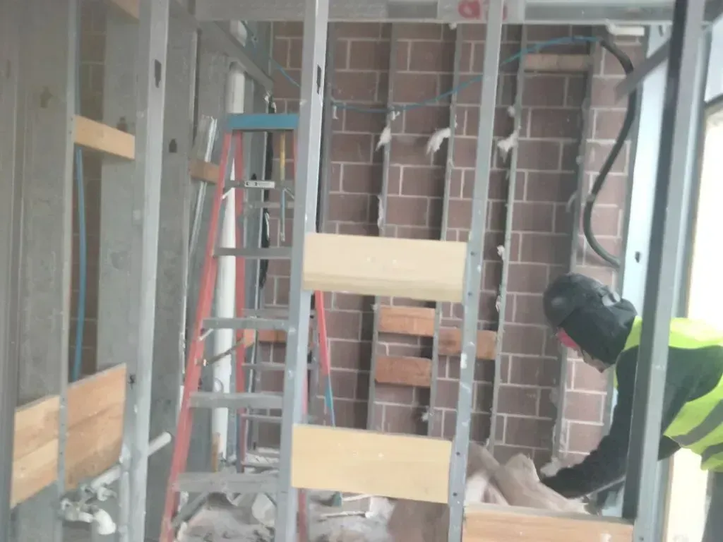 A construction worker in a high-visibility vest works inside an unfinished building frame with exposed brick walls.