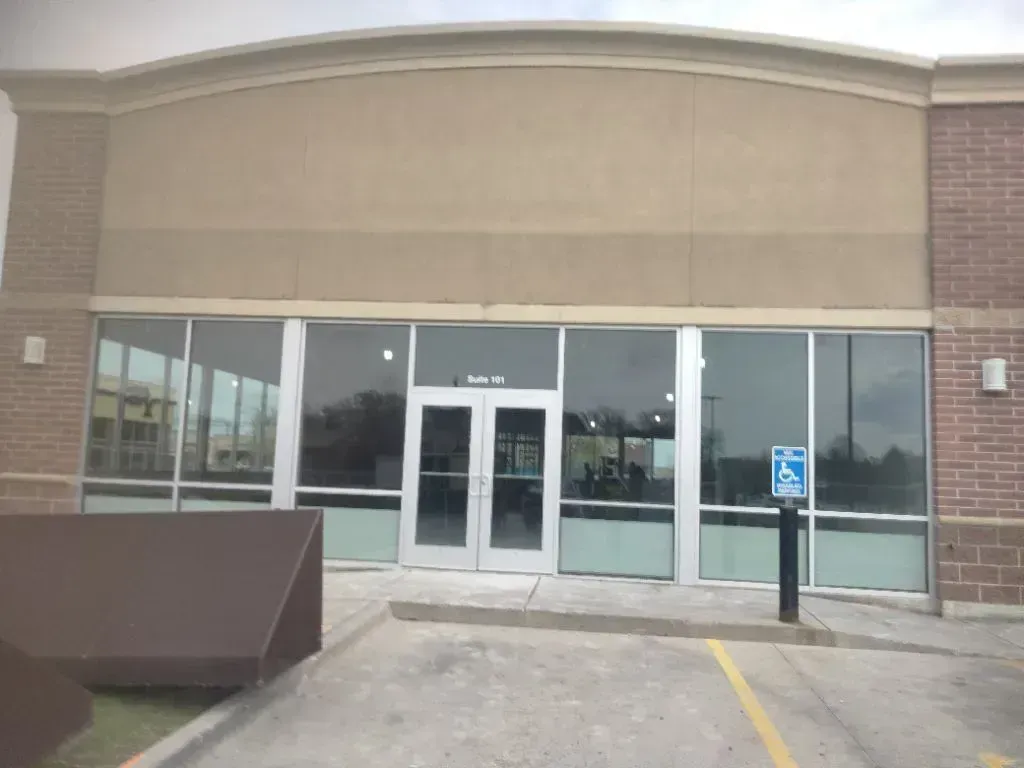 A tan-colored commercial storefront with glass doors and windows, a brick facade, and a blue handicap parking sign.