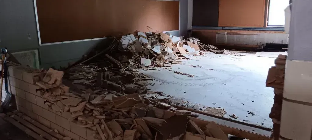 A room under renovation with a partially demolished brick wall and a pile of rubble on the floor.