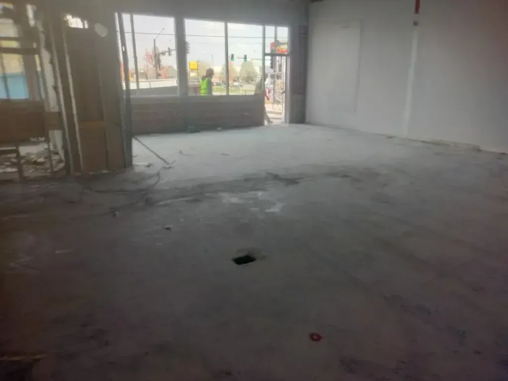 An empty commercial space under construction with a concrete floor, framed walls, and large windows looking outside.