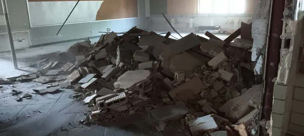 A pile of grey concrete rubble and construction debris inside a dimly lit building interior.