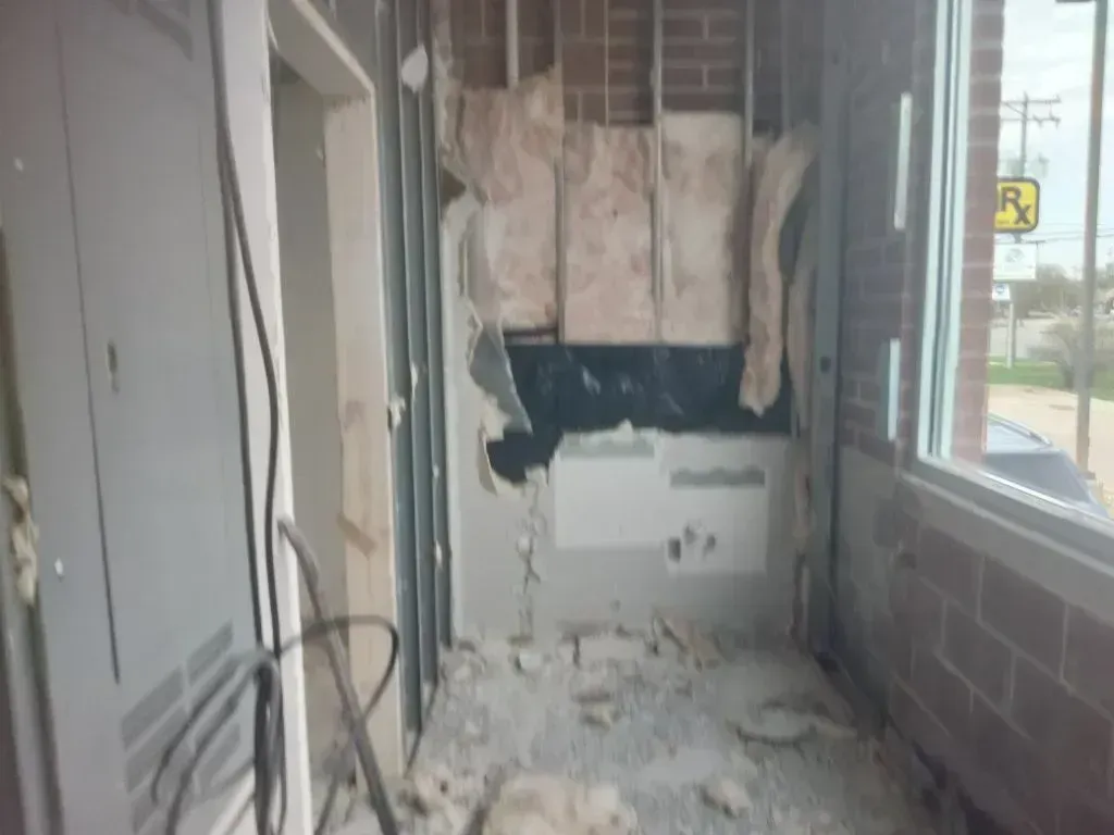 A construction site interior showing an exposed wall frame with insulation, debris on the floor, and a nearby window.