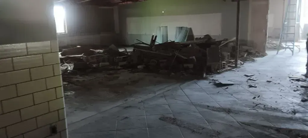 An interior view of a room under renovation with tiled floors, debris, exposed materials, and bright light from a window.