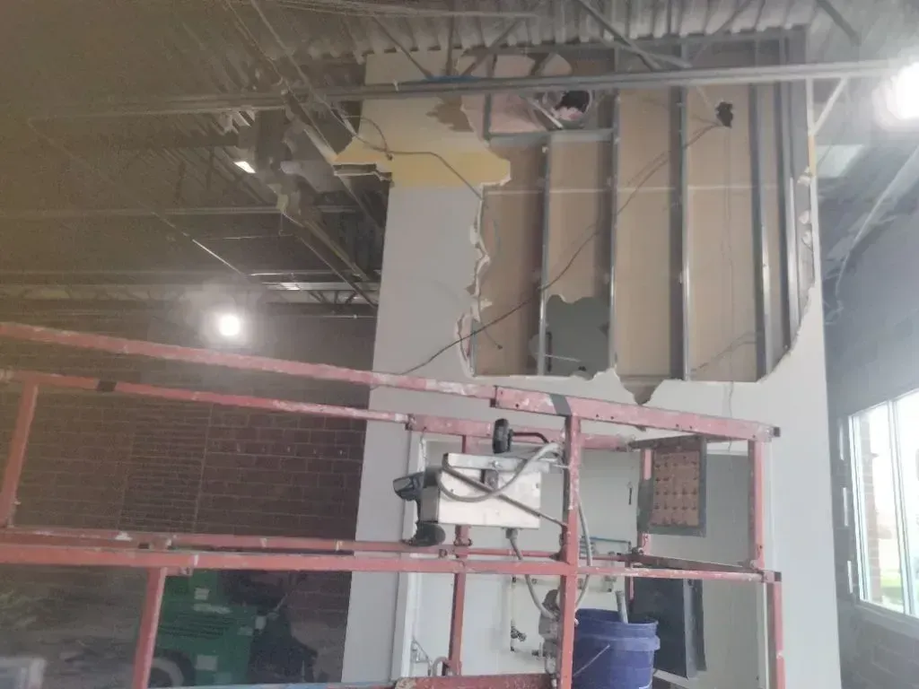 Interior view of a construction site showing a wall with missing drywall exposing metal studs and a red scaffolding unit.
